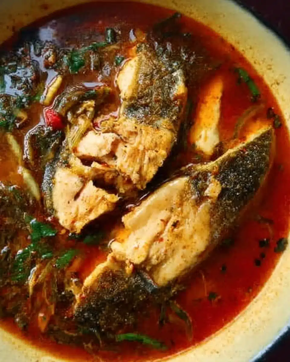 Bowl of spicy Fish Pepper Soup garnished with herbs and peppers