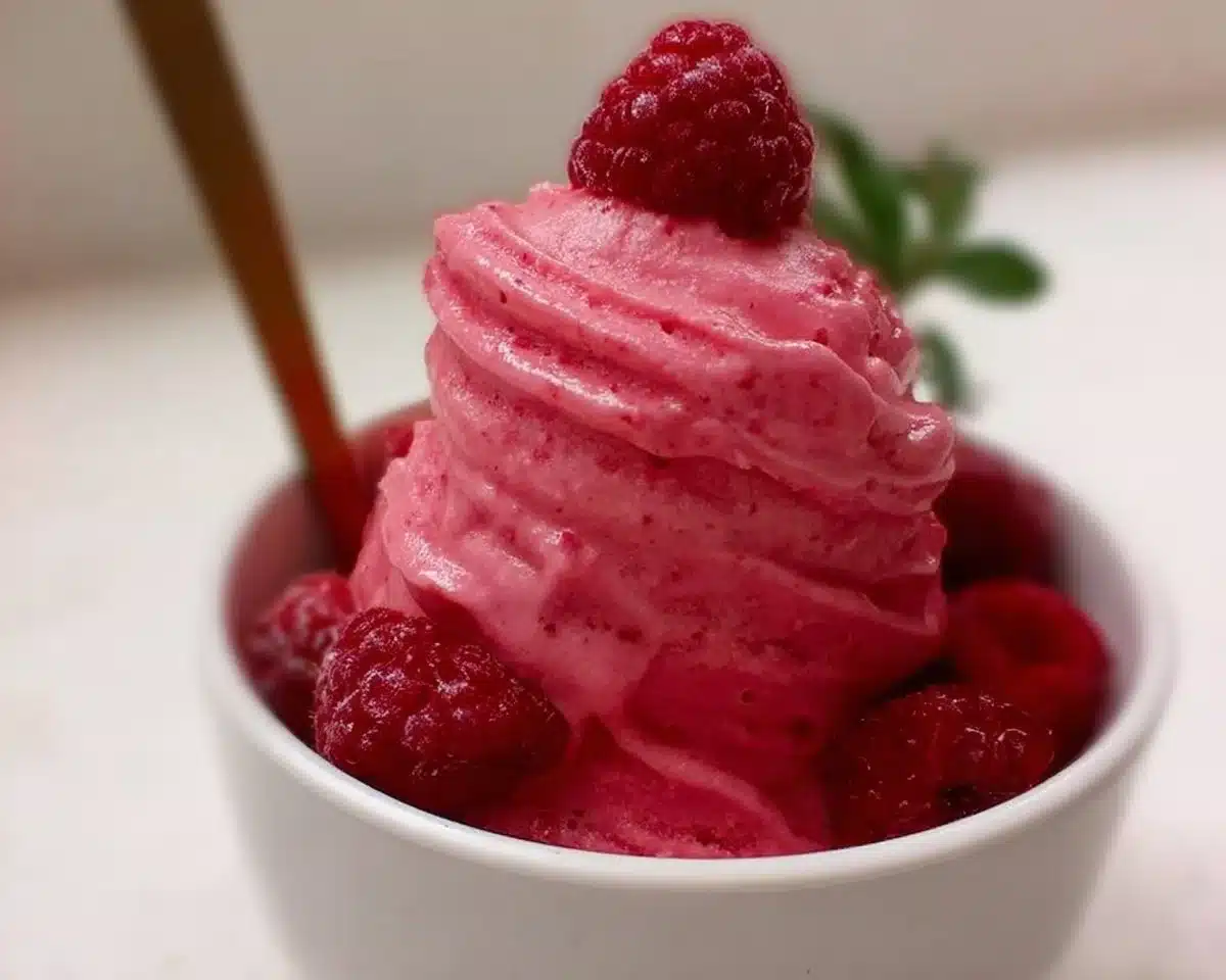 Creamy raspberry frozen yogurt in a bowl with fresh raspberries on top